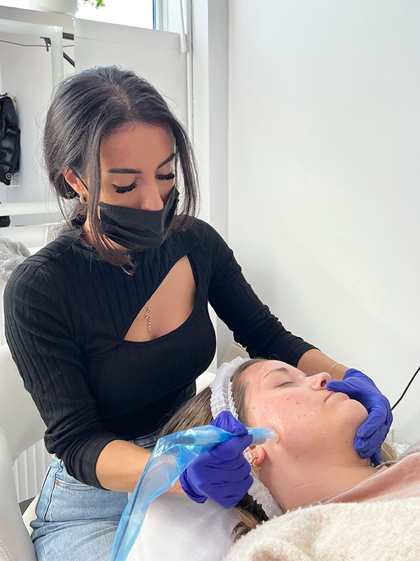 Beauty by Maria V - Lash Extensions Esthetics and Training - Maria microneedling a client wearing gloves and a mask using edermastamp tool